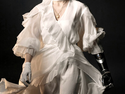 A woman in a white dress shirt and gold necklace, equipped with a high-tech robotic arm