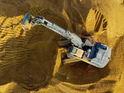 An excavator positioned on a sandy mound, reflecting the beginning of site adaptation and ground conditioning