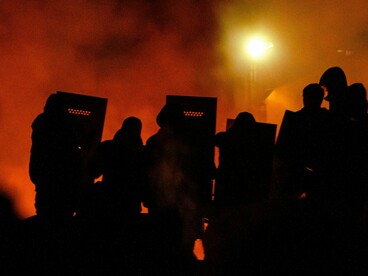 Blazing streets lit by orange and red flames as crowds gather, reflecting the combustible nature of civil unrest