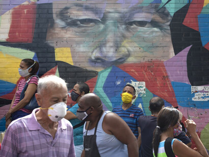 Venezolanos caminan por la calle durante la pandemia frente a un mural de Hugo Chávez