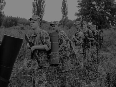 In a single file line, military men march through the grass, armed