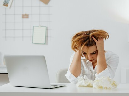 A woman resting her head in her hand while sitting before her laptop, symbolising the mental exhaustion created by overthinking and uncertainty