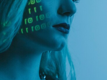 Sequências binárias são projetadas sobre o rosto de uma mulher. Os dados que alimentam a inteligência artificial podem reproduzir padrões e preconceitos presentes na sociedade. O artigo analisa como vieses sociais podem ser incorporados aos sistemas de IA. A aparente neutralidade dos algoritmos nem sempre corresponde à realidade dos dados utilizados no seu treino