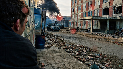 A shattered city street bears the scars of conflict, as smoke rises in the distance and silence settles over the ruins of everyday life