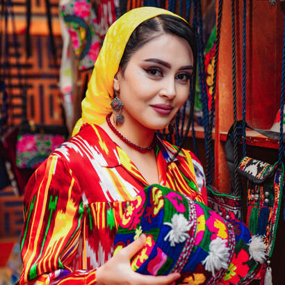 In Uzbekistan, a woman wearing a yellow headscarf holds a vibrant, handcrafted round bag—a reflection of the country’s rich artistic traditions