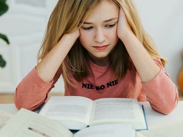 A girl with her head in her hands, bored yet still trying to read as meaning slips away