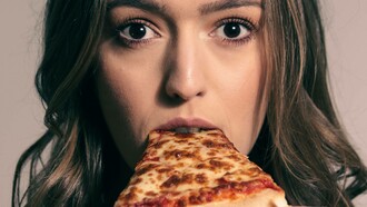 A woman looks shocked as she takes a bite of a slice of pizza