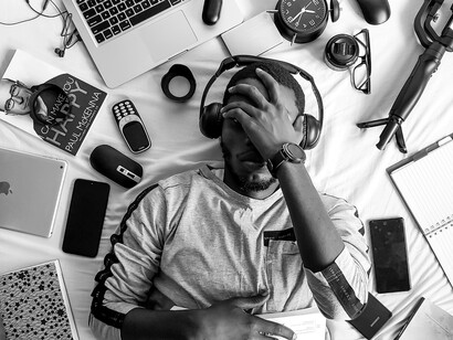 A man lies on his bed in frustration, surrounded by technology