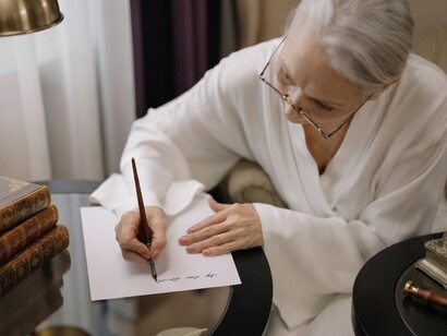A senior woman reflects on her memories as she writes a personal letter with a fountain pen