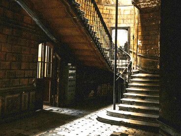 A dark, decaying interior, where broken tiles fracture the floor at the foot of a narrow staircase