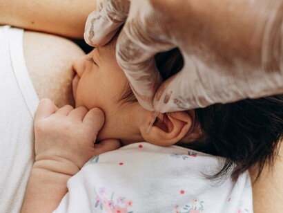 Mãe amamenta o bebê enquanto recebe o apoio de outra pessoa que segura sua mão. A amamentação envolve não apenas a alimentação, mas também cuidado, proximidade e vínculo