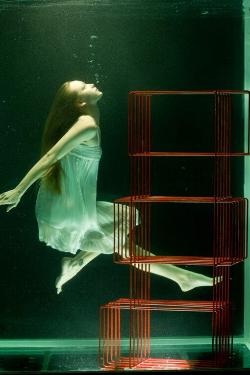 A woman submerged in water, staring up at a red bookcase, captured in a digital surrealist style