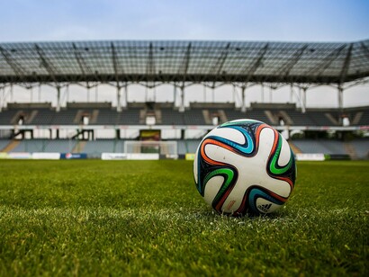 Em primeiro plano, uma bola de futebol se destaca sobre a grama, enquanto o estádio aparece desfocado ao fundo. É dentro desse cenário que as decisões de treinador, jogadores e diretoria precisam transformar expectativa em resultados