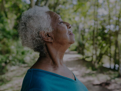 An older woman taking calming breaths in a serene woodland setting, embracing the tranquility of nature