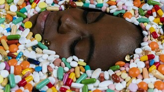 A woman's face is surrounded by scattered multivitamins, symbolizing the overwhelming presence of supplements in daily health routines