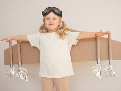 A front-view of a girl, delightfully engaged with cardboard wings, embodies the spirit of imagination, dreams, and the pursuit of success