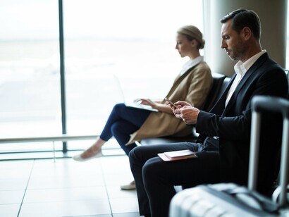 Waiting to board, a businessman checks his phone while a professional works on her laptop, showcasing the importance of staying connected and organized while traveling