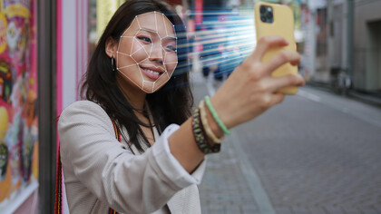 Facial recognition technology illustrated by a woman holding a phone with scanning lines across her face