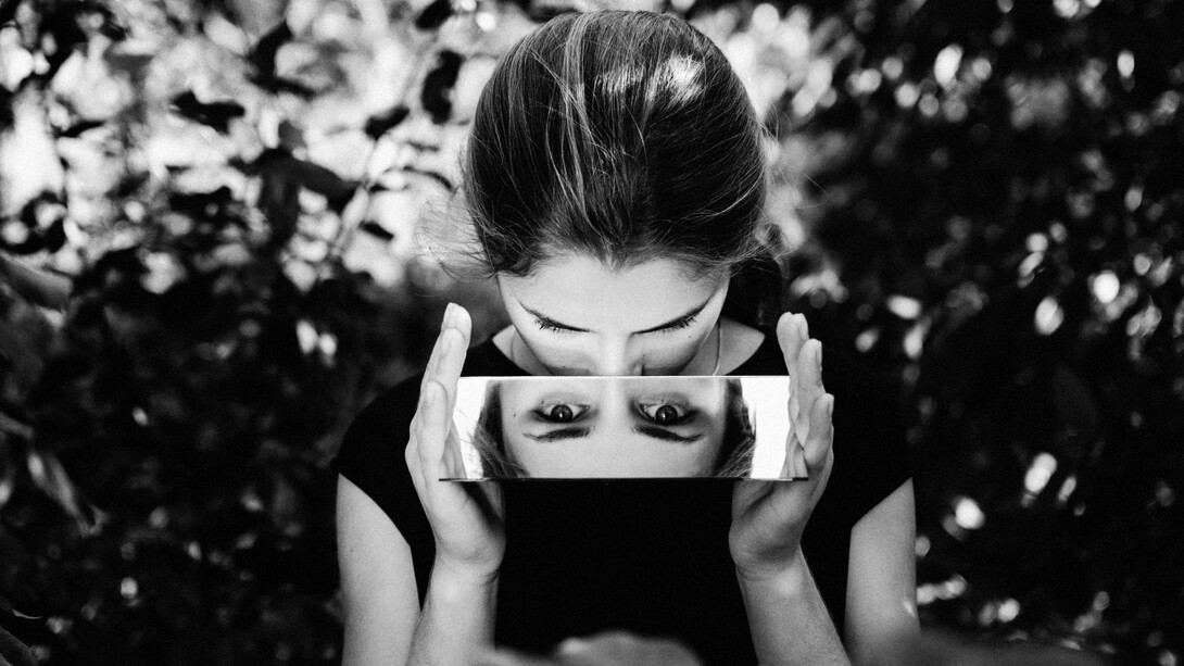 A woman stares into the camera through a mirror held in her hands