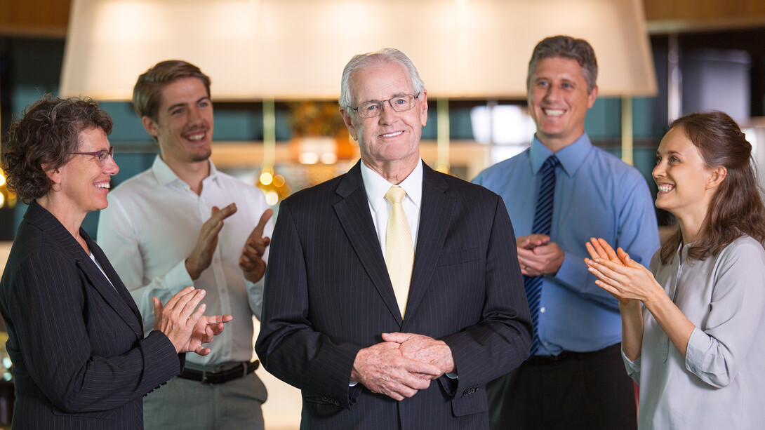 An experienced leader standing confidently before colleagues, proud and smiling