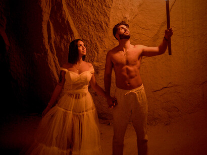 In the quiet secrecy of a cave, two lovers meet under the warm, wavering light of a torch