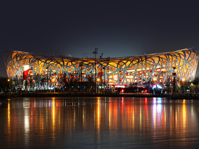 The illuminated Beijing National Stadium at night, designed by Herzog & de Meuron for the 2008 Olympics. Known as the “Bird’s Nest,” the stadium is a striking example of biomimicry in architecture, with its interwoven steel structure inspired by the natural form of a bird’s nest, Beijing, China