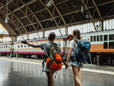 Duas mulheres seguem pela estação com mochilas nas costas, em meio ao movimento de uma viagem que já começou. Quando o medo está relacionado ao desconhecido, avançar passo a passo pode ser também uma forma de aprender que é possível partir, viver a experiência e retornar
