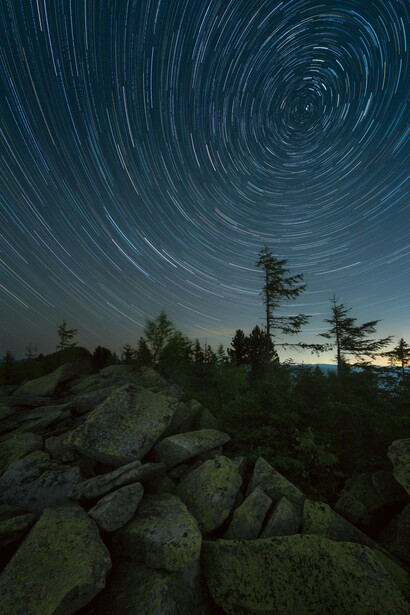 Time-lapse photography of lights on a mountain at night, with galaxies, stars, and the vast universe overhead