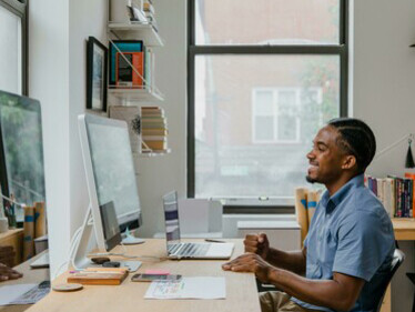 A man talks on the phone while working at his desk in a home office