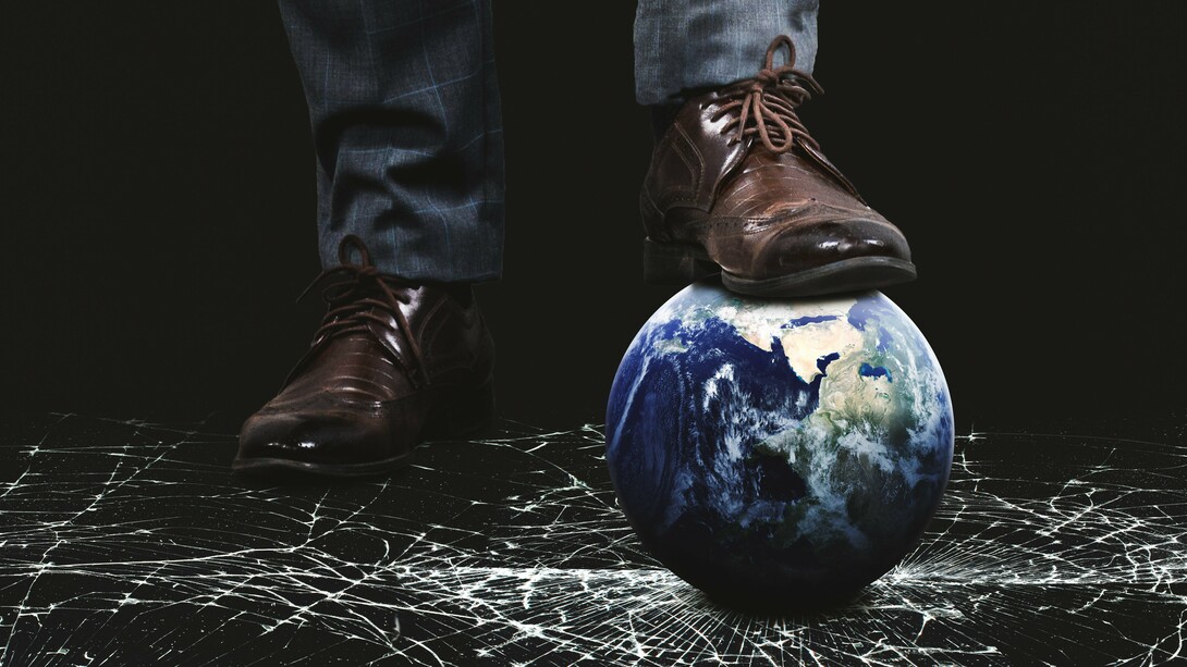 A foot standing on a globe, crushing it against a surface of shattered glass—a stark reminder of the consequences of unchecked power and the urgent need for renewed global solidarity