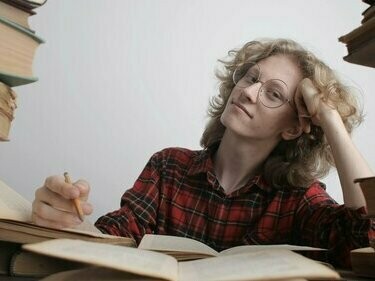 Homem escreve em meio à pilha de livros. Devemos nos preocupar menos com a existência da IA e mais com a falta de letramento digital crítico. Se tantas pessoas têm dificuldade em diferenciar uma fonte confiável de desinformação online, o problema está na formação, não na ferramenta. Seria como culpar um bisturi por erros cometidos por um cirurgião despreparado