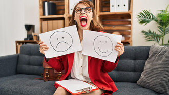 A young woman is holding papers with an unhappy face in one hand and a happy face in the other
