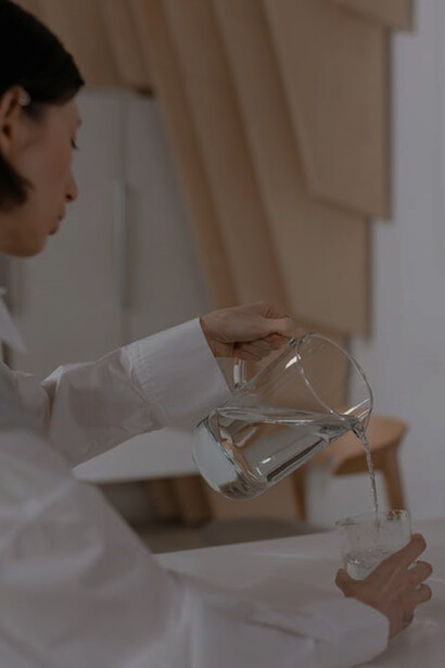 A woman is gracefully pouring water from a jug into a glass