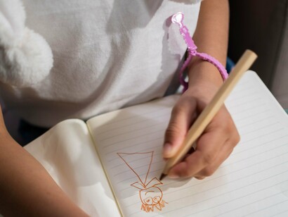 Uma menina desenha atentamente sobre uma folha branca, concentrada nos traços que começa a construir no papel. No texto, o desenho da família se transforma em um momento de descoberta: diante do espaço reservado ao pai, falta à criança uma referência para continuar o traço