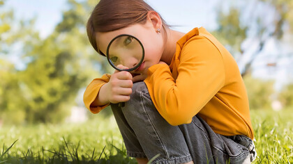 A small girl is using a magnifying glass to explore her surroundings and solve problems