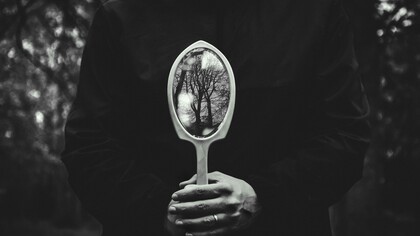 A person holding a hand mirror toward the autumn forest, reflecting shifting perspectives
