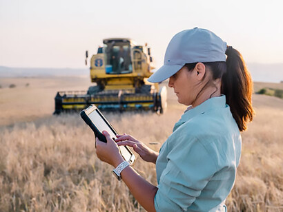 A female farmer stands in a farm field holding a digital tablet, using smart farming technology
