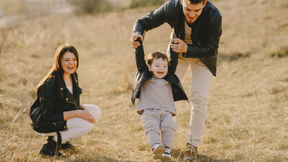 Mãe e pai levam o filho para brincar no campo de forma que aproveitem uma paisagem mais natural e ar puro
