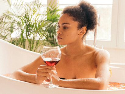 A woman holds a glass while resting her arms on a bathtub