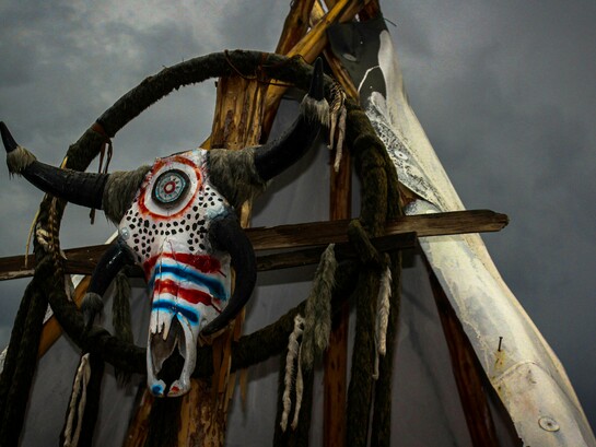 A ceremonial bull skull fixed upon a rustic wooden frame beneath a turbulent sky in Mexico, reflecting the lingering presence of ancestral belief systems