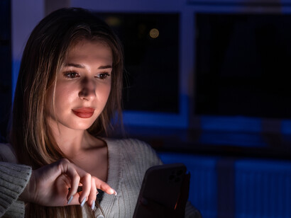 A young woman sits on the stairs in the evening, illuminated by blue light from her smartphone, reflecting digital addiction
