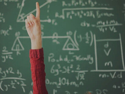 A student confidently raising their hand against a green board in a classroom serves as a contrasting example to the concepts advocated by Rousseau