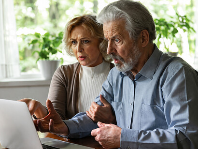A distressed elderly couple looks shocked while reading fraudulent information on their computer at home
