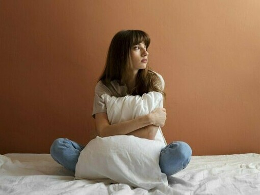 A young woman gazing into the distance while clutching a pillow, reflecting the search for hope beyond fear