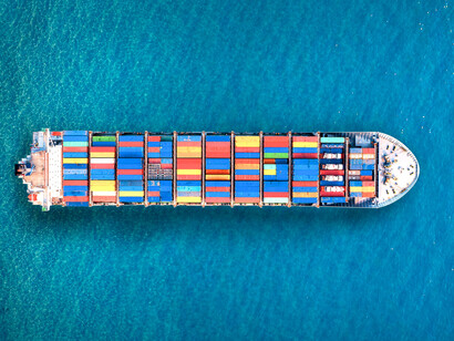 An aerial view of a cargo ship sailing through the ocean, symbolising the flow of goods sustaining global economies