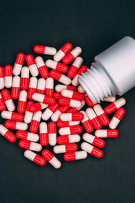 High-angle view capturing red-and-white capsule drugs cascading from a small pill bottle
