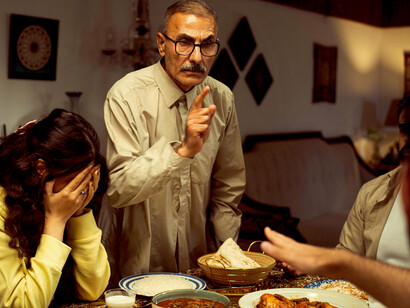 A tense family disagreement unfolds around the dinner table during an indoor gathering