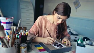 Woman painting a desk next to pots of paint and pencils