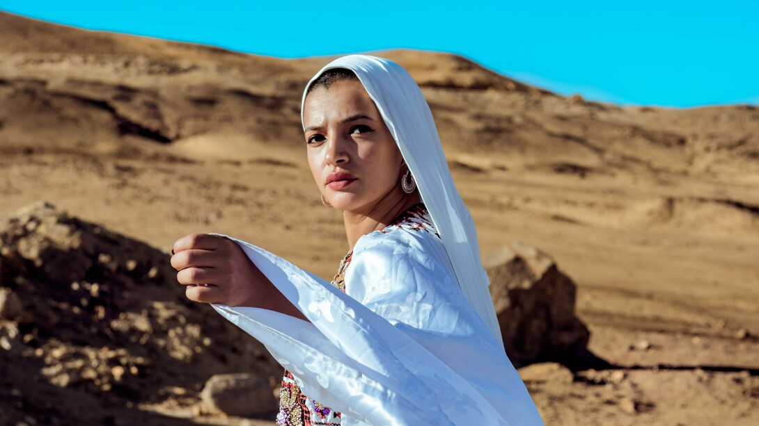 A woman wearing flowing white traditional attire against a desert landscape, representing cultural identity shaped by heritage and place