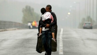 Un refugiado siriio carga con su hija bajo la lluvia al llegar a Grecia